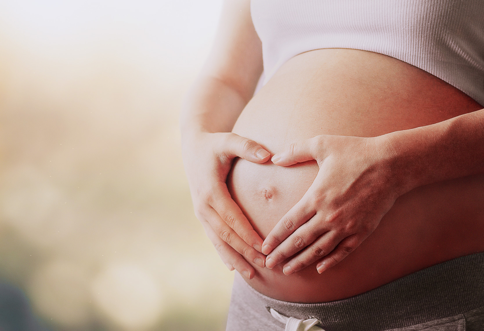 pregnant woman's belly with fingers heart symbol
